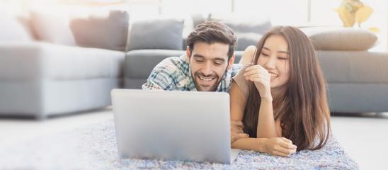 Glückliches junges Paar liegt vor dem Laptop auf dem Wohnzimmerteppich