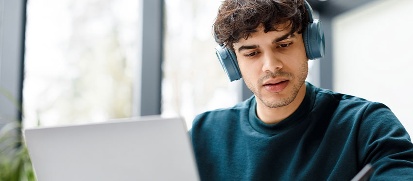 Junger Mann mit Kopfhörer sitzt vor Laptop