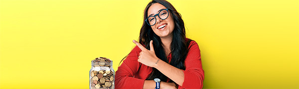 Dunkelhaarige junge Frau mit Brille zeigt lachend nach links oben. Neben ihr steht ein Glas mit Geldmünzen