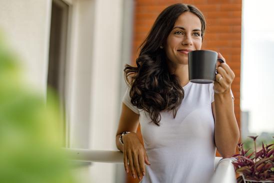 Frau steht entspannt auf ihrem Balkon.