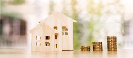 Nachfinanzierung Haus: Kleines Hausmodelle aus Holz mit daneben stehendem, aufsteigendem Münzstapel.