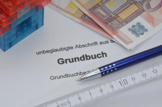 Grundbuchabschrift mit Stift, Geldscheinen und Modellhäuschen