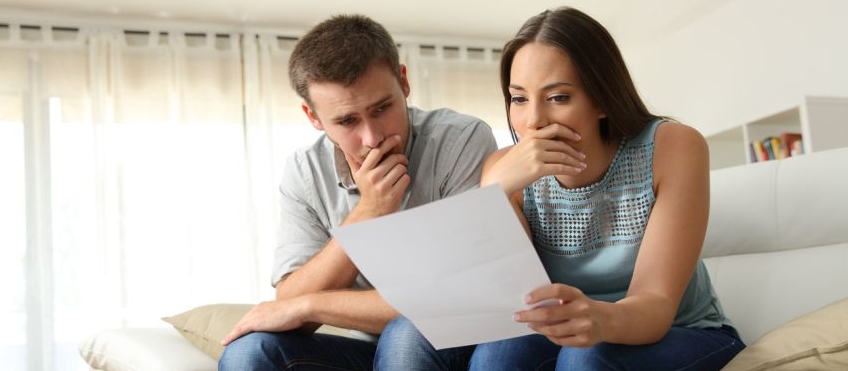 Nachdenkliches Paar sitzt auf Sofa mit Blatt Papier in der Hand
