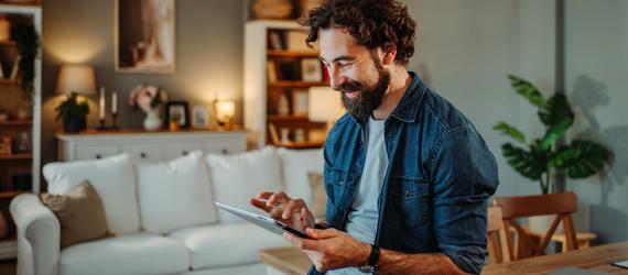 Lächelnder Mann im Wohnzimmer nutzt ein Tablet