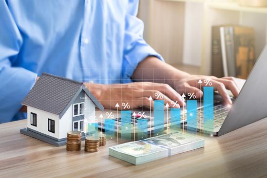 Effektiver Jahreszins: Mann tippt in Laptop, davor eine Zinskurve und ein Hausmodell
