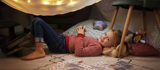 Mädchen liegt mit Kissen und Stofftieren in ihrer "Räuberhöhle"