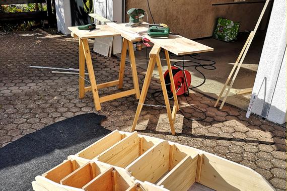 Ein Holzregal liegt auf dem Boden, weitere Bretter und Arbeitsgeräte liegen daneben auf Holzböcken