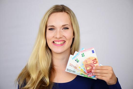 Junge Frau hält lächelnd Geldscheine in der Hand.
