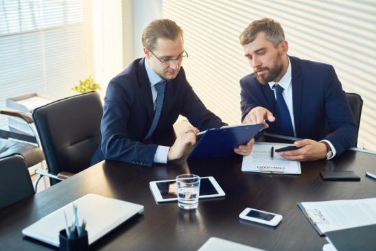 Concentrated thoughtful businessmen discussing contract terms and reading it together in board room