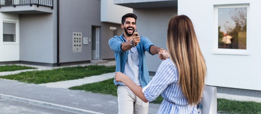 Bausparvertrag-Sonderzahlung: Paar freut sich vor Haus, Mann hält den Schlüssel in der Hand