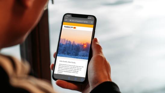 Mann hält Handy mit Newsletter in der Hand