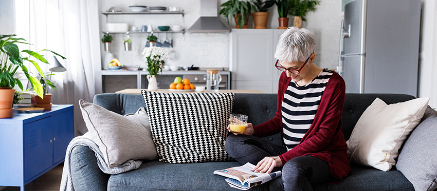 Frau sitzt auf Sofa und liest eine Zeitschrift