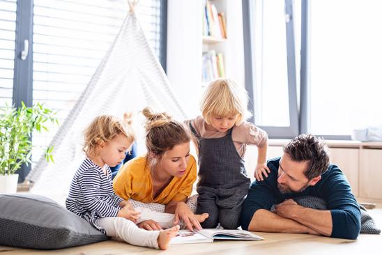 Ratgeber Wohnglück – Tipps für ein schönes Zuhause Familie mit zwei Kindern schaut sich auf dem bodenliegend ein Buch an
