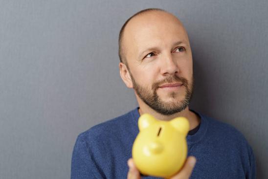 Mann hält Sparschwein in der Hand und überlegt