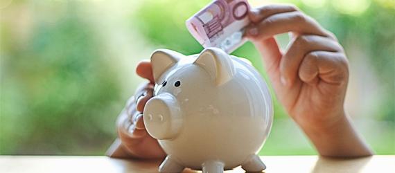 Hand steckt 10-Euro-Schein in ein Sparschwein