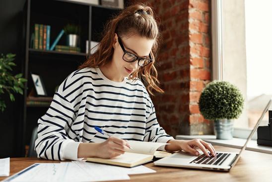 Junge Frau sitzt am Notebook und macht sich Notizen.