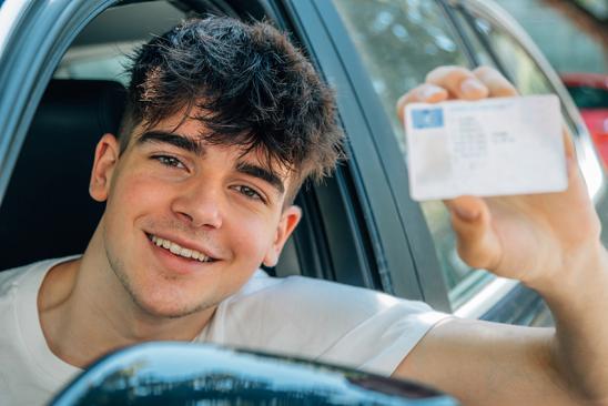 Junger Mann sitzt im Auto und zeigt seinen Führerschein.