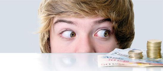 Junge schaut über die Tischkante und schielt nach rechts zu einem Stapel Geldscheinen und Münzen