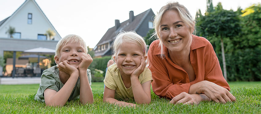 Lächelnde Frau und zwei Kinder liegen auf dem Ellbogen gestützt im Rasen