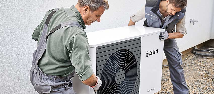 Zwei Männer installieren eine Wärmepumpe vor einem Haus.