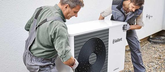 Zwei Männer installieren eine Wärmepumpe vor einem Haus.