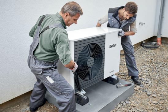 Zwei Männer installieren eine Wärmepumpe vor einem Haus.