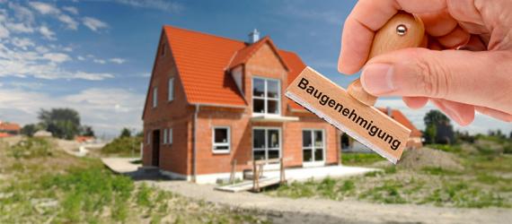 Stempel mit der Aufschrift Baugenehmigung, im Hintergrund ein Neubau