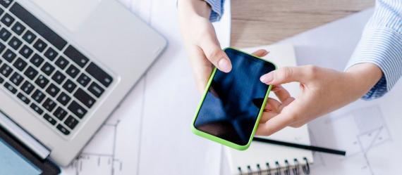 Mobiltelefon in Händen gehalten und ein Laptop auf Schreibtisch