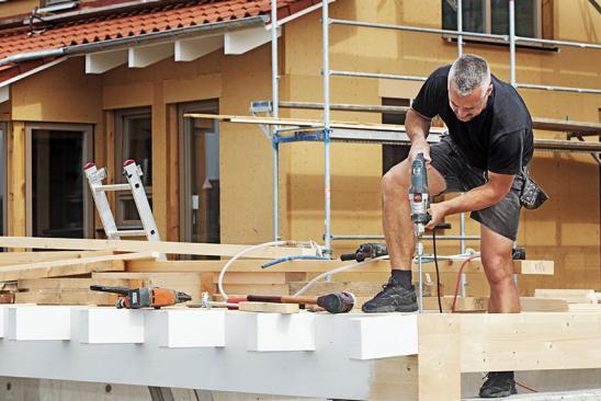 Handwerker bohrt stehend auf Holzkonstruktion