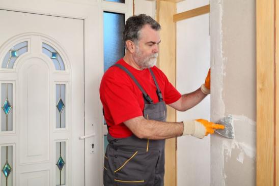 Worker spreading plaster with trowel to gypsum board and fiber mesh