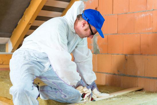 Handwerker schneidet Material, um Dachboden zu dämmen.