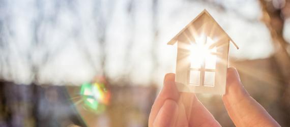 Prolongation: Hand mit Modellhaus im Gegenlicht