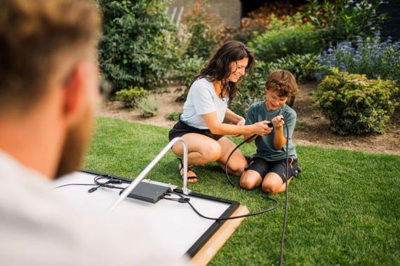 Mutter und Kind verbinden Solarmodule eines Balkonkraftwerkes mit dem Wechselrichter