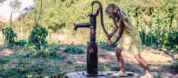 Mädchen bedient Schwengelpumpe im Garten