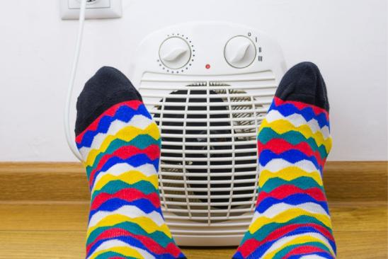 Kalte Füße in bunten Socken vor einem elektrischen Heizlüfter