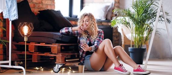 Junge Frau sitzt auf dem Boden und blickt aufs Mobiltelefon