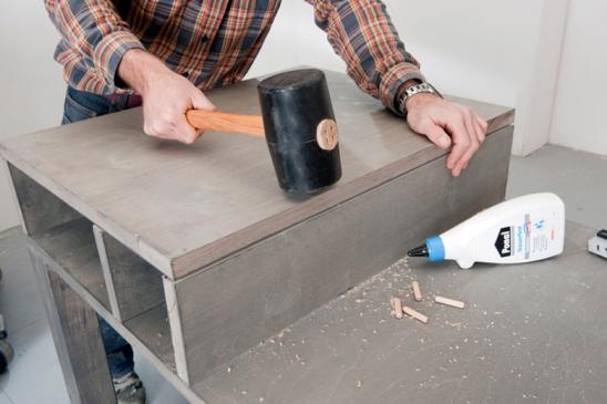 Grilltisch: Mann passt mit Gummihammer verklebte Holzteile an