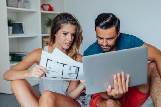 Young couple is using laptop pc while woman is holding architecture plans