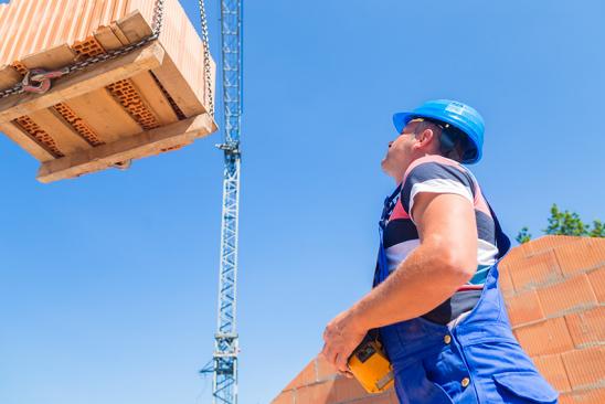 Arbeiter auf einer Baustelle verlädt Palette per Kran.