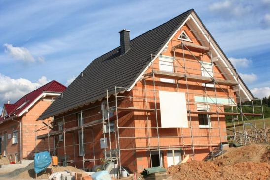Modernes Einfamilienhaus im Rohbau mit Baugerüst, blauer Himmel und Sonnenschein