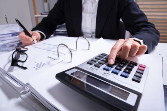 Midsection Of Businessperson Calculating Invoice With Calculator And Bills On Desk