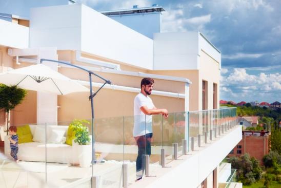 Junger Mann steht am Glasgeländer der Dachterrasse und genießt die Aussicht