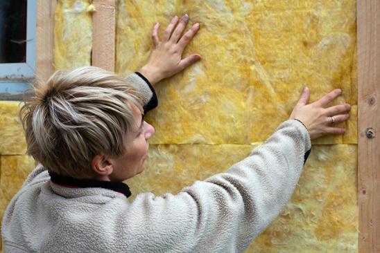 Frau bringt Außendämmung an einer Fassade an
