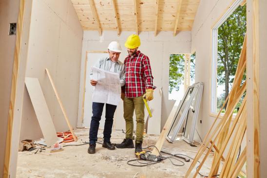 Haus günstig sanieren: Handwerksmeister und Handwerker schauen auf Bauplan
