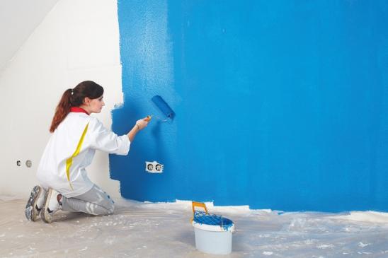 Frau streicht Zimmerwand mit Farbwalze blau