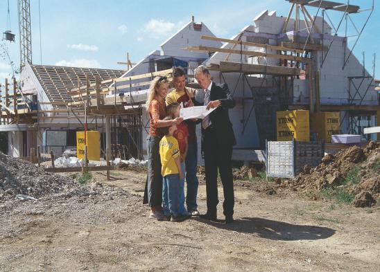 Familie steht vor Eigenheim-Baustelle und bespricht Pläne