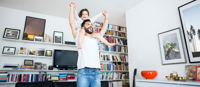 Vater mit Kind auf den Schultern steht im Wohnzimmer