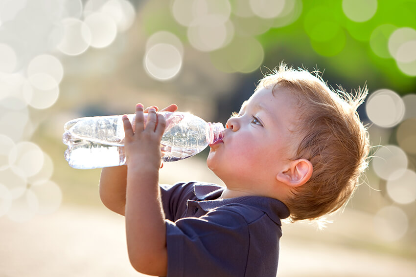 Kleiner blonder Junge trinkt aus Wasserflasche
